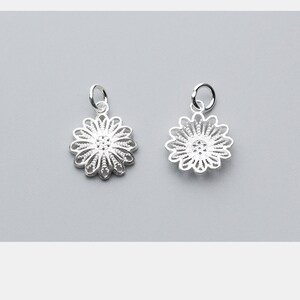 May include: Two silver charm pendants in the shape of a delicate, intricate flower with a circular center. The charms have a loop at the top for attaching to a necklace or bracelet.