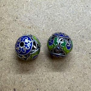 Può includere: Due perline rotonde in argento con intricati disegni in smalto blu e verde. Le perline hanno un foro al centro per essere infilate.