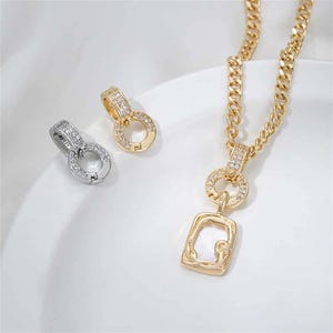 May include: A gold necklace with a square pendant featuring a clear crystal and two smaller circles with clear crystals. The necklace has a chain link design. There is also a silver version of the pendant shown in the image.