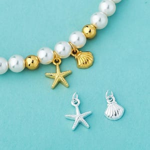 May include: A beaded bracelet featuring white spherical beads interspersed with smaller gold-toned metallic spheres. Two gold-toned charms, a starfish and a seashell, hang from the beads. Below, a silver-toned starfish charm and a silver-toned seashell charm.