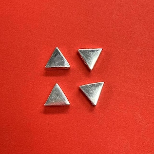 Puede incluir: Cuatro abalorios de plata en forma de triángulo sobre un fondo rojo.