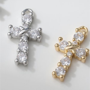 May include: Two cross pendants, one silver-toned and one gold-toned, each adorned with sparkling, clear gemstones. The crosses feature a classic design with rounded edges and a loop at the top for hanging. The gemstones are round and set closely together.