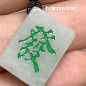May include: A green jade mahjong tile pendant with a white background and a green inscription. The tile has a hole at the top for a cord or chain.
