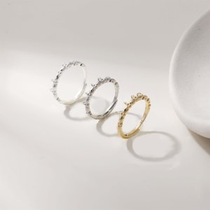 May include: Three rings in silver and gold, each with a repeating branch design. The rings are displayed on a white surface. One ring is gold, and two are silver, showcasing a delicate, nature-inspired aesthetic.