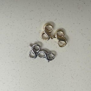 Puede incluir: Dos juegos de cierres de metal dorado y plateado en forma de la letra "S".