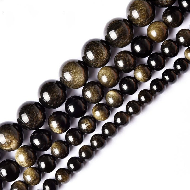 May include: A strand of black and gold beads with a shimmering, iridescent finish. The beads are round and smooth, and they are arranged in a graduated size, with the largest beads at the top and the smallest beads at the bottom.