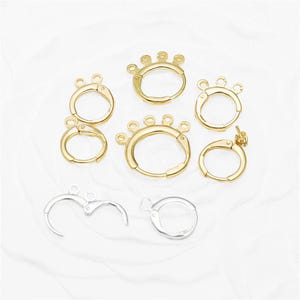 May include: A selection of gold and silver earring findings. The gold components feature hoop-style clasps with decorative details. The silver findings are plain hoop clasps. All are presented on a white surface.
