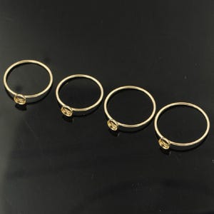 May include: Four gold-colored ring blanks with small bezel settings. The rings are arranged on a black surface. These jewelry findings are ideal for creating custom rings with gemstones or other embellishments.