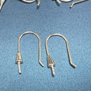 May include: Two silver earring hooks with a pointed end. The hooks are made of metal and have a smooth finish.