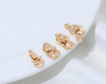 May include: Four gold-toned metal lobster claw clasps arranged in a row. Each clasp features a textured surface and is accented with a small, clear, round embedded stone. The clasps include a spring-loaded mechanism and a small attached jump ring.