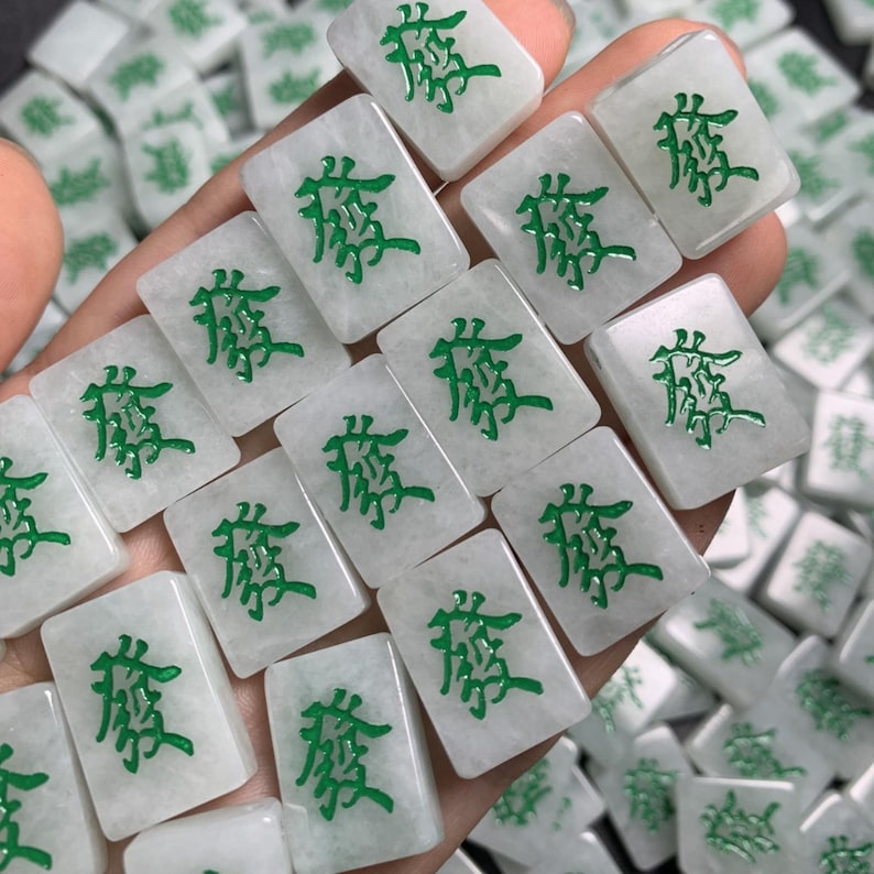 May include: A close-up of a set of white jade mahjong tiles with green Chinese characters. The tiles are arranged in a hand, with the characters facing up.
