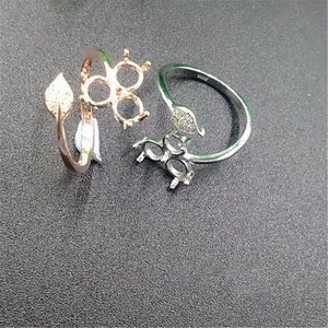Puede incluir: Dos anillos de plata con un diseño de hoja y tres engastes abiertos para piedras. Un anillo es de oro rosa con un diseño de hoja y tres engastes abiertos para piedras.