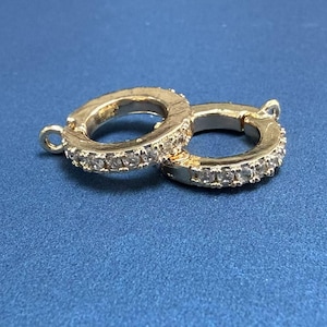 May include: A pair of gold-toned hoop earrings with a row of clear cubic zirconia stones around the edge of each hoop.