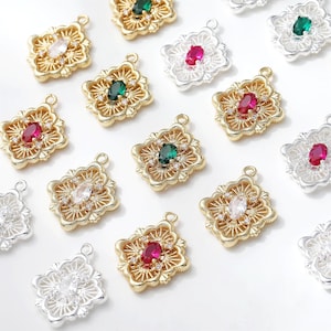 Puede incluir: Una colección de dijes de metal para joyería en forma cuadrada con intrincados patrones de filigrana, cada uno centrado con una piedra preciosa de corte ovalado en rojo, verde o transparente, y acentuado con pequeñas piedras claras, en acabados dorados y plateados.