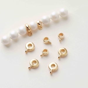 Op de afbeelding: Gouden metalen kralencaps met een ronde vorm en een kleine lus aan de onderkant. De kralencaps zijn gerangschikt op een wit oppervlak.