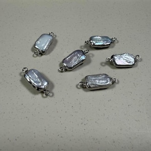 May include: Six silver-toned rectangular pearl connectors with two loops on each side. The pearls are iridescent white.