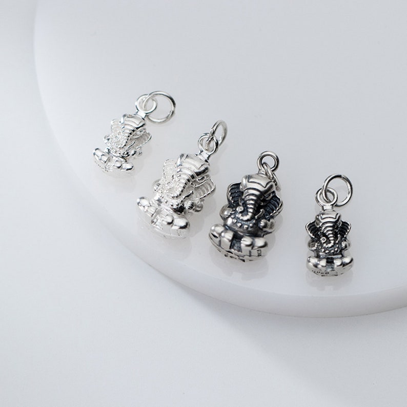 May include: Four silver charms in the shape of a seated elephant deity. The charms are different sizes and have a loop at the top for attaching to a necklace or bracelet.