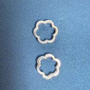 May include: Two silver flower-shaped charms with a smooth, shiny finish. The charms are hollow and have a circular opening in the centre.