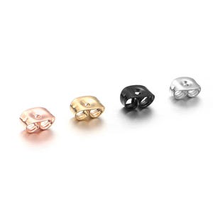 May include: Four earring backs in different colors: rose gold, gold, black, and silver. Each back has two prongs for secure attachment.