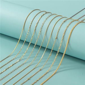 May include: A collection of gold-colored necklaces displayed against a light blue background. The necklaces feature various chain styles, including snake chains, twisted rope chains, and beaded chains. The chains are arranged in a diagonal pattern, showcasing their different designs.