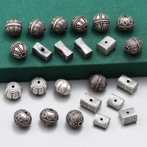 May include: A collection of silver-toned metal beads with various intricate designs. The beads are round and have a smooth, polished finish. Some beads have a textured surface.