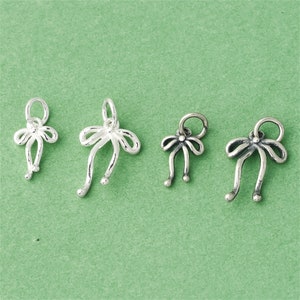 Op de afbeelding: Vier zilveren strikcharms met een lus aan de bovenkant om aan een armband of ketting te bevestigen.
