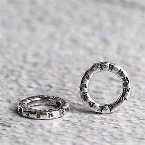 Puede incluir: Dos anillos de plata con diseños intrincados e inscripciones alrededor de la banda. Los anillos son lisos y brillantes.