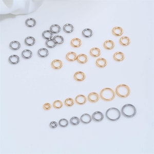 May include: A collection of small metal jump rings in gold and silver tones. The rings vary in size, with some arranged in rows and others scattered. The jump rings are used for jewelry making and other crafts.
