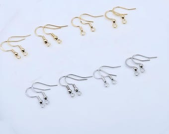 Puede incluir: Una colección de ganchos para pendientes de metal dispuestos en dos filas. La fila superior presenta cuatro pares de ganchos dorados, mientras que la fila inferior muestra cuatro pares de ganchos plateados, cada uno con una pequeña cuenta.