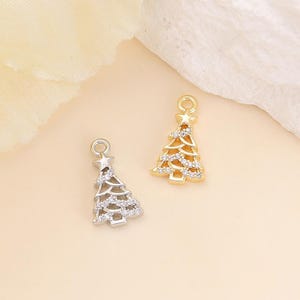 May include: Two Christmas tree charms, one silver-toned and one gold-toned, each with a star on top and encrusted with small, clear crystals. The charms are designed for jewelry making or holiday crafts.