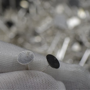 Peut inclure: Deux disques m&eacute;talliques argent&eacute;s &agrave; surface textur&eacute;e, tenus par un tissu blanc. Les disques sont petits et ronds, et semblent &ecirc;tre d&eacute;coratifs ou fonctionnels.