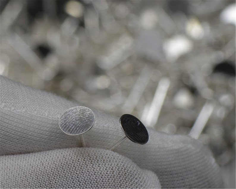 Peut inclure: Deux disques m&eacute;talliques argent&eacute;s &agrave; surface textur&eacute;e, tenus par un tissu blanc. Les disques sont petits et ronds, et semblent &ecirc;tre d&eacute;coratifs ou fonctionnels.
