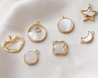 May include: A collection of gold-colored charms in various shapes, including a heart, circle, star, and clover. Each charm features a white, iridescent inlay and a small loop for attaching to jewelry. Some charms have a small clear gem.