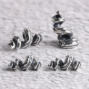 Può includere: Quattro perline argentate a forma di spirale. Le perline hanno una finitura strutturata e ossidata, con un design dettagliato e vorticoso. Le perline sono esposte su una superficie grigio chiaro. Queste perline sono adatte per la creazione di gioielli.