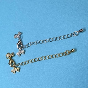 May include: Two silver and gold chain extenders with clear crystal accents. The extenders are made of metal and have a lobster clasp closure.