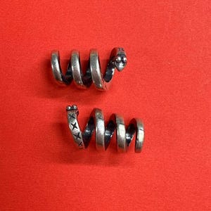 May include: Two silver spiral hair cuffs. One cuff has a snake head design at the end. The other cuff has a cross design at the end.