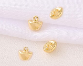 May include: Four gold-colored charms. Two charms are shaped like ingots with a loop at the top for attaching to jewelry. The other two charms are oval-shaped with a loop on the back. The charms are on a white fabric background.