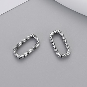 May include: Two silver-toned oval-shaped connectors featuring a twisted rope-like texture. Each link has a visible hinge mechanism on one side, allowing the oval to open and close. The metal surface has a polished finish with darkened recessed areas.