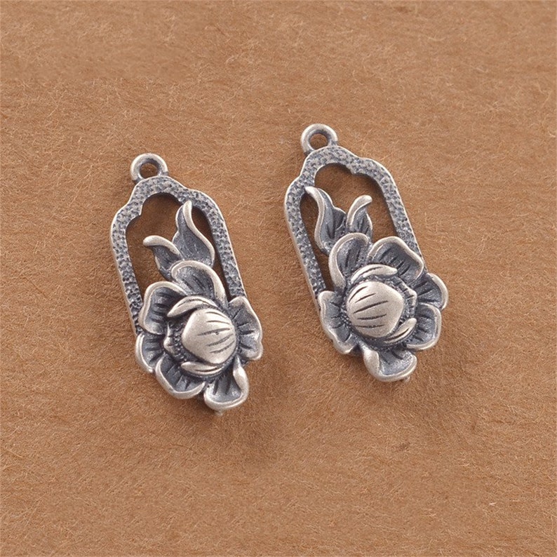 May include: Two silver-toned flower charm pendants with intricate floral designs. The charms are shaped like a rectangle with a floral design inside. The charms are perfect for adding a touch of elegance to jewellery projects.