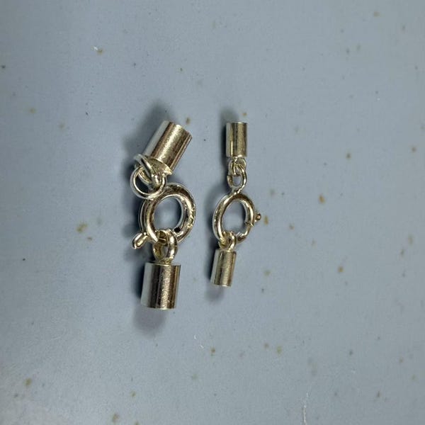 May include: Two silver-toned metal clasps for jewellery making. Each clasp has a round ring and a barrel-shaped end.