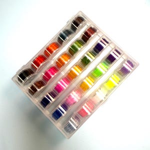 May include: A clear plastic organizer filled with colorful thread spools. The spools are arranged in rows and display a variety of colors, including red, orange, pink, green, and purple. The thread is tightly wound on the spools.