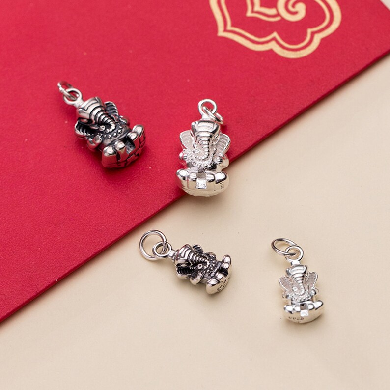 May include: Four silver charms in the shape of the Hindu deity Ganesha. The charms are detailed and have a textured finish.