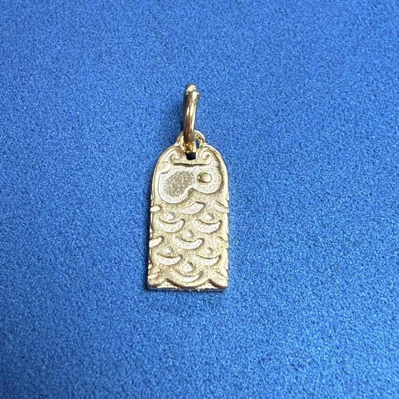 May include: Gold-colored pendant charm featuring an owl design. The owl has a detailed, textured body and a simple face with eyes.