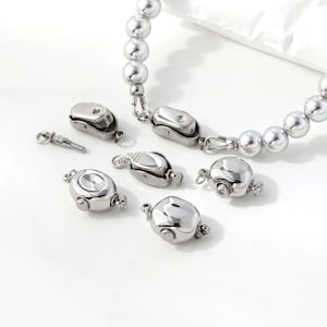 May include: A collection of silver-toned metal magnetic jewelry clasps with a smooth, polished finish. The set includes several oval-shaped magnetic closures and a partial beaded necklace strand featuring a matching clasp mechanism.