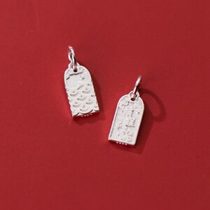 May include: Two silver charms, one with a fish design and the other with Chinese characters. The charms are on a red background.