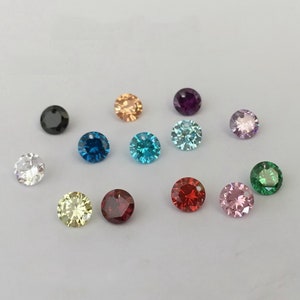 Puede incluir: Surtido de piedras preciosas redondas y facetadas en varios colores, incluyendo negro, blanco, azul claro, azul oscuro, turquesa, rosa claro, rojo, verde, amarillo y naranja. Las piedras preciosas están dispuestas sobre una superficie blanca.