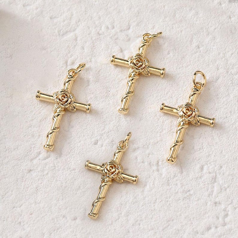 May include: Four gold-tone cross charms with a rose design. Each cross charm has a loop at the top for attaching to a necklace or bracelet.