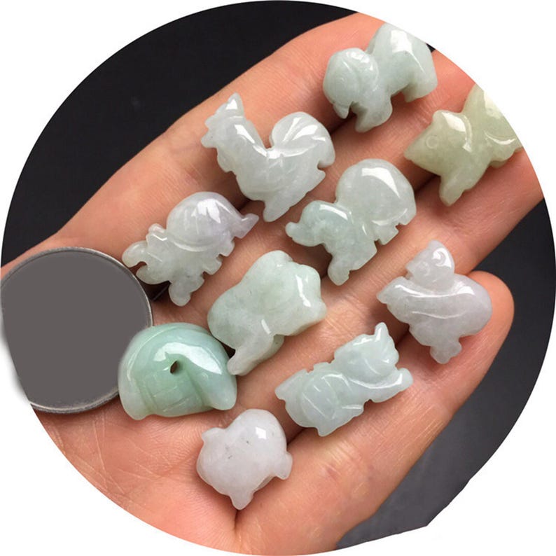 Pode incluir: Uma cole&ccedil;&atilde;o de pequenas figuras de animais em jade esculpido, incluindo um galo, uma tartaruga e um porco. As figuras s&atilde;o principalmente verde claro com alguns detalhes roxos e brancos. A cole&ccedil;&atilde;o &eacute; segurada em uma m&atilde;o.