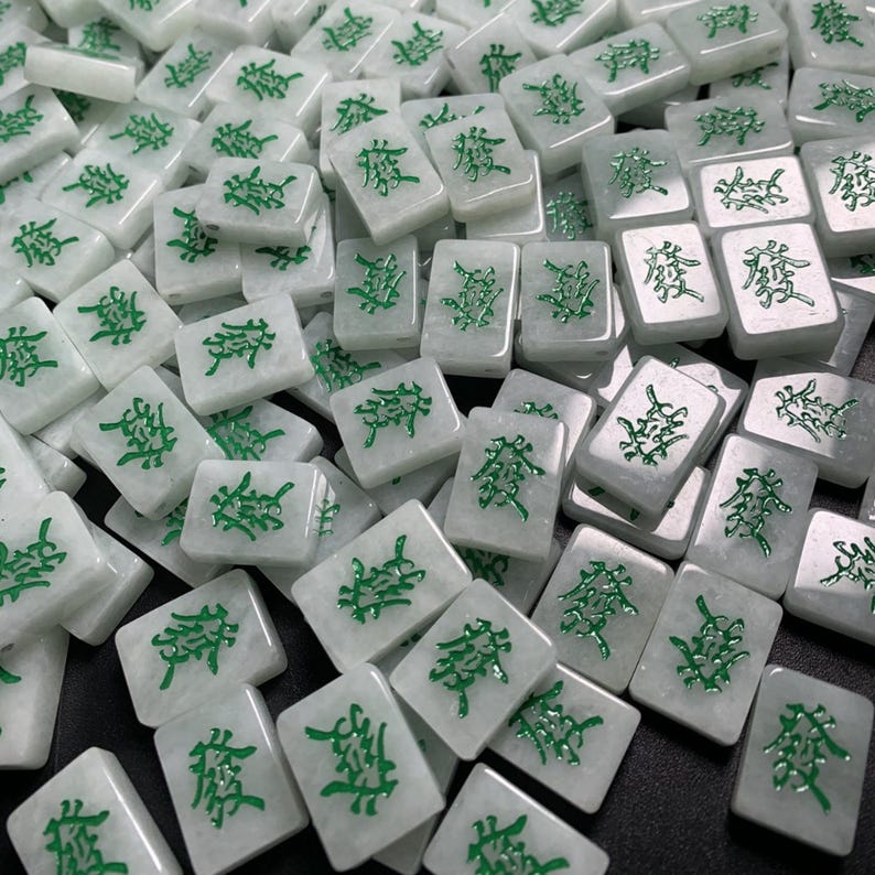May include: A close-up of a pile of white mahjong tiles with green Chinese characters. The tiles are arranged in a random pattern.