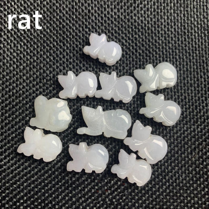 Pode incluir: Uma cole&ccedil;&atilde;o de pequenas figuras de rato esculpidas em jade em v&aacute;rias poses. As figuras s&atilde;o de uma cor verde-branca p&aacute;lida e transl&uacute;cida e est&atilde;o dispostas sobre uma superf&iacute;cie texturizada cinza escuro. A palavra "rat" est&aacute; no canto superior esquerdo.